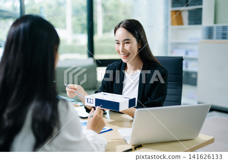 Professional Asian real estate consultant presenting a house model to a client during a property investment meeting in a modern office. 141626133