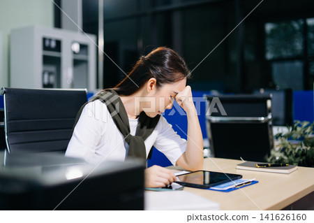 Asian woman feeling migraine head strain.Overworked businesswoman financier while working on laptop and tablet at office. Asian woman feeling migraine head strain.Overworked businesswoman financier while working on laptop and tablet at office. 141626160