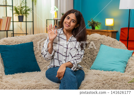 Indian woman waving hello friendly hand greeting toward camera happy smile positive gesture indoor Indian woman waving hello friendly hand greeting toward camera happy smile positive gesture indoor 141626177