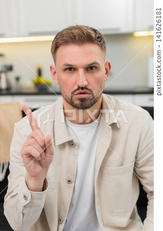 Young man waves finger no no at camera shows firm refusal and disagree sign with serious calm face Young man waves finger no no at camera shows firm refusal and disagree sign with serious calm face 141626181