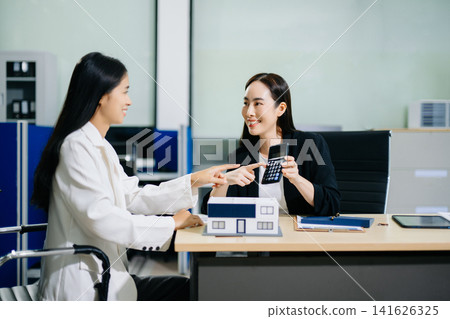 Real estate broker agent presenting and consult to customer to decision making sign insurance form agreement, home model, concerning mortgage loan offer in office Real estate broker agent presenting and consult to customer to decision making sign insurance form agreement, home model, concerning mortgage loan offer in office 141626325