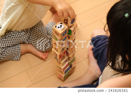 A child's hands playing with building blocks, stacking them high at home. 141626381