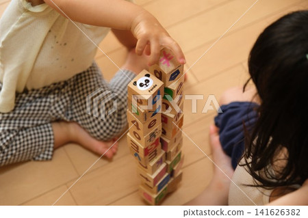 A child's hands playing with building blocks, stacking them high at home. A child's hands playing with building blocks, stacking them high at home. 141626382