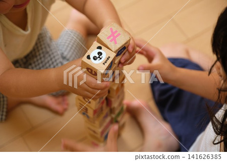Two children playing with building blocks, stacking them high at home. Two children playing with building blocks, stacking them high at home. 141626385