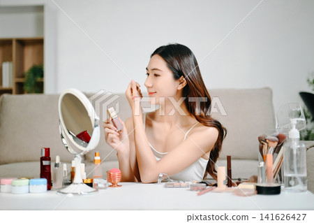 Asian beauty influencer filming a makeup tutorial using cosmetics, skincare products, smartphone and ring light in a modern home studio for social media content. Asian beauty influencer filming a makeup tutorial using cosmetics, skincare products, smartphone and ring light in a modern home studio for social media content. 141626427