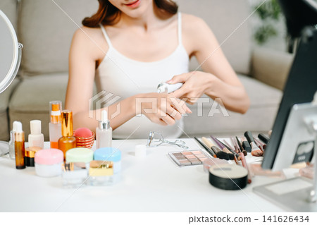 Closeup of a young Asian woman holding a pink lipstick tube at her makeup table, capturing a serene moment in her daily self care routine. Closeup of a young Asian woman holding a pink lipstick tube at her makeup table, capturing a serene moment in her daily self care routine. 141626434