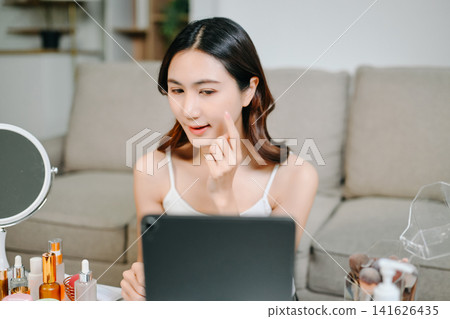 Asian beauty influencer filming a makeup tutorial using cosmetics, skincare products, smartphone and ring light in a modern home studio for social media content. Asian beauty influencer filming a makeup tutorial using cosmetics, skincare products, smartphone and ring light in a modern home studio for social media content. 141626435