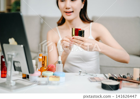 Asian woman carefully applies lipstick in front of a vanity mirror, highlighting her daily beauty and makeup routine. 141626447