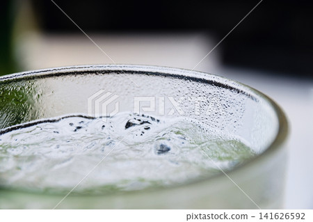 Close up of condensation on a clear glass filled with refreshing ice cold liquid beverage Close up of condensation on a clear glass filled with refreshing ice cold liquid beverage 141626592