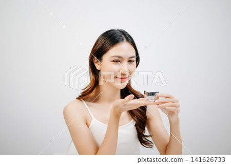 Asian woman presenting skincare product with clean minimal aesthetic, glowing skin and beauty routine concept for cosmetic advertising 141626733