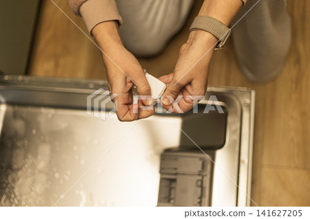 Woman unwrapping dishwasher detergent tablet before loading kitchen appliance Woman unwrapping dishwasher detergent tablet before loading kitchen appliance 141627205