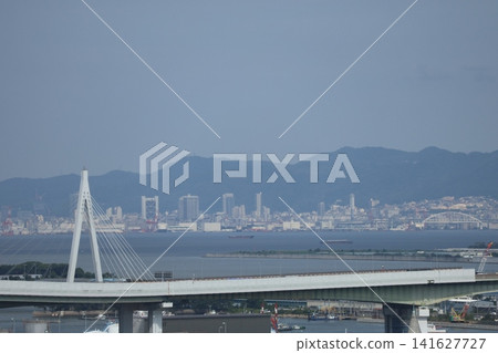 Blue sky, mountain range, cityscape on the opposite shore, the sea, highway bridge, and waterfront townscape. Blue sky, mountain range, cityscape on the opposite shore, the sea, highway bridge, and waterfront townscape. 141627727