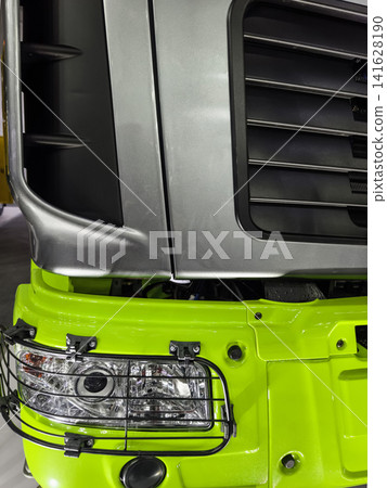 Truck showing part of the front with a green and silver design in a workshop during daylight 141628190