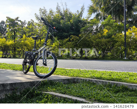 Folding Bicycle Parked on a Sunny Sidewalk 141628479