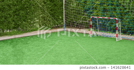 Photo of a small mini-football field with an artificial synthetic turf, on which a red and white goal with nets is installed, playground. Empty copy space Photo of a small mini-football field with an artificial synthetic turf, on which a red and white goal with nets is installed, playground. Empty copy space 141628641