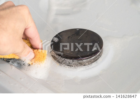 Photo of manual cleaning of the surface of a gas stove from small dirt with a cleaning agent and a greenhouse household sponge Photo of manual cleaning of the surface of a gas stove from small dirt with a cleaning agent and a greenhouse household sponge 141628647