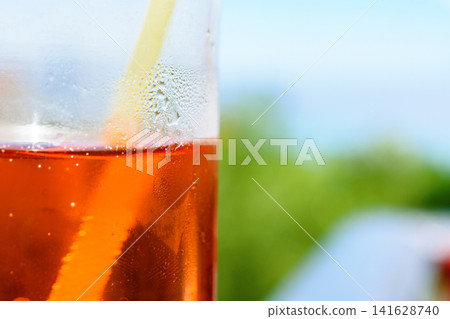Close up of an orange cocktail with ice and a yellow straw with condensation on a sunny background Close up of an orange cocktail with ice and a yellow straw with condensation on a sunny background 141628740
