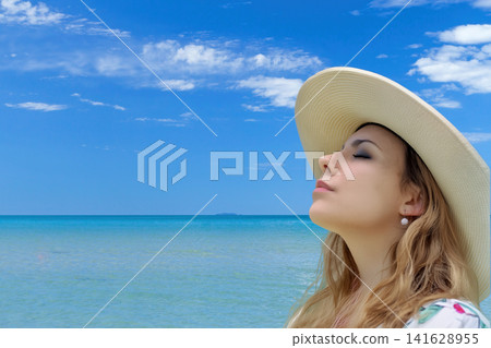 Young woman in a straw hat relaxing on the seashore Young woman in a straw hat relaxing on the seashore 141628955