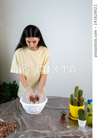 Young Woman Holding Expanded Clay Pebbles Over Bowl For Cactus Repotting Young Woman Holding Expanded Clay Pebbles Over Bowl For Cactus Repotting 141629021