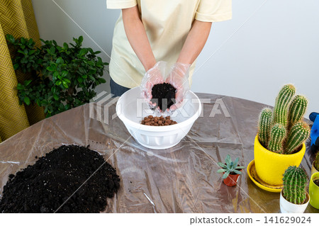 Woman in Gloves Holding Handful of Dark Soil Above Potting Bowl 141629024