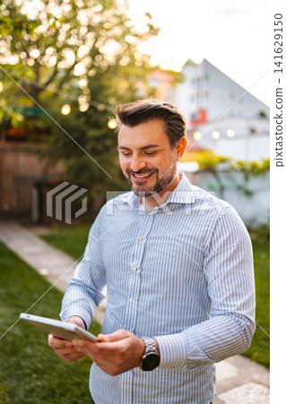 Smiling man using digital tablet in warm backyard light Smiling man using digital tablet in warm backyard light 141629150