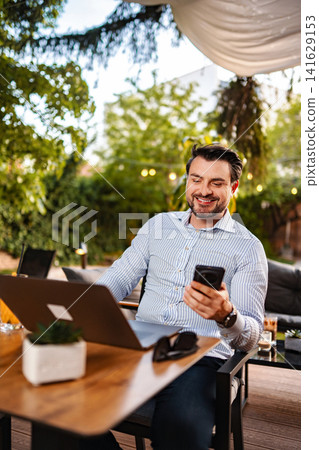 Young adult man working outdoors using laptop and phone Young adult man working outdoors using laptop and phone 141629153