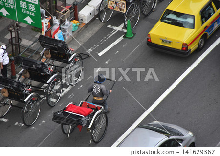 在日本東京淺草,淺草寺附近的一條道路上停放著許多人力車。一位戴著草帽的車夫正牽著其中一輛人力車。 在日本東京淺草,淺草寺附近的一條道路上停放著許多人力車。一位戴著草帽的車夫正牽著其中一輛人力車。 141629367