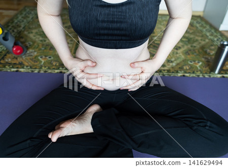 Woman demonstrating belly fat before doing yoga for weight loss and breathing exercises. Concept of body positivity, self love, and home fitness. Woman demonstrating belly fat before doing yoga for weight loss and breathing exercises. Concept of body positivity, self love, and home fitness. 141629494