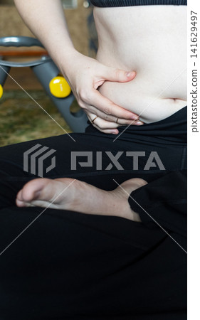 Woman demonstrating belly fat before doing yoga for weight loss and breathing exercises. Concept of body positivity, self love, and home fitness. Woman demonstrating belly fat before doing yoga for weight loss and breathing exercises. Concept of body positivity, self love, and home fitness. 141629497