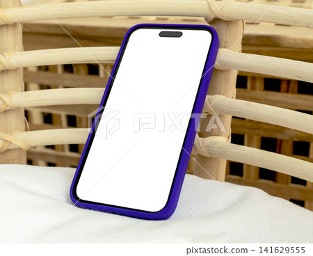 Blank smartphone mockup in purple case on wicker basket. Angled mobile phone with copy space for app design and advertising. Clean product background for technology presentation.. Blank smartphone mockup in purple case on wicker basket. Angled mobile phone with copy space for app design and advertising. Clean product background for technology presentation.. 141629555