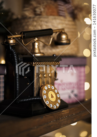 Antique black rotary phone in festive interior with warm lighting of golden garland lights Antique black rotary phone in festive interior with warm lighting of golden garland lights 141630077