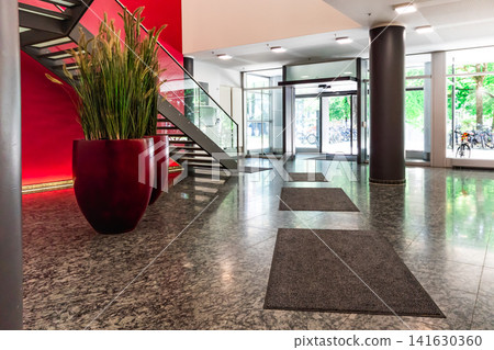 Modern office lobby with red feature wall and glass staircase, contemporary corporate interior with granite floor, cylindrical columns and large plant pots Modern office lobby with red feature wall and glass staircase, contemporary corporate interior with granite floor, cylindrical columns and large plant pots 141630360