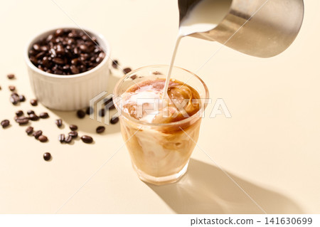 Pouring milk into ice coffee Pouring milk into ice coffee 141630699