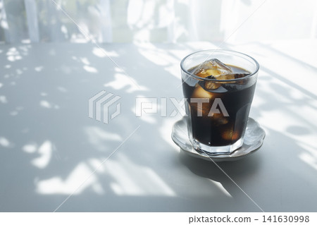 陽光斑駁地灑在桌上,一杯冰咖啡擺在那裡——這是一幅令人神清氣爽的夏日咖啡館景象。 陽光斑駁地灑在桌上,一杯冰咖啡擺在那裡——這是一幅令人神清氣爽的夏日咖啡館景象。 141630998