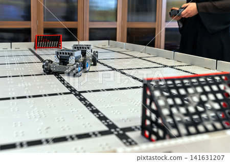Two small robots compete on a classroom grid, showcasing technology. Two small robots compete on a classroom grid, showcasing technology. 141631207