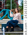 Young Woman Posing Elegantly on Steps by Modern Art Installation in Urban Setting 141631530