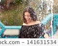 Joyful Woman Playing in Splashing Water at Outdoor Park in Bright Sunshine 141631534
