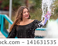 Joyful Woman Playing in Splashing Water at Outdoor Park in Bright Sunshine 141631535