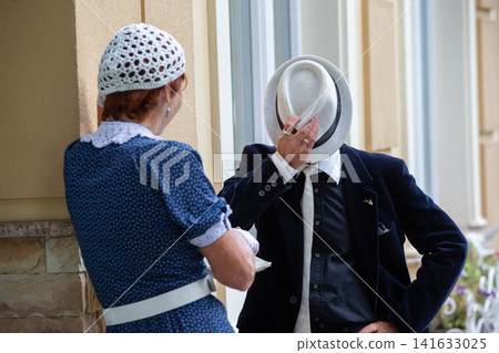 Couple engaged in conversation outdoors while dressed in vintage attire under soft daylight Couple engaged in conversation outdoors while dressed in vintage attire under soft daylight 141633025