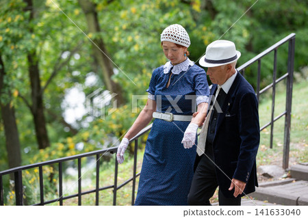 Elderly couple walking hand in hand through a park during autumn, dressed in vintage attire, enjoying a peaceful afternoon 141633040