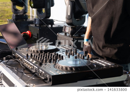 Outdoor DJ setup with controller, laptop, headphones and performer beside stage gear, cables and sound equipment during live music event in daylight, with dj, music, background, authentic detail Outdoor DJ setup with controller, laptop, headphones and performer beside stage gear, cables and sound equipment during live music event in daylight, with dj, music, background, authentic detail 141633800