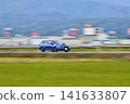A blue station wagon speeding through the countryside. 141633807