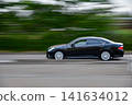 A panning shot of a black car speeding through lush greenery. 141634012
