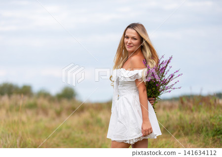 Young woman in white dress holding flowers in a green field on a cloudy day Young woman in white dress holding flowers in a green field on a cloudy day 141634112