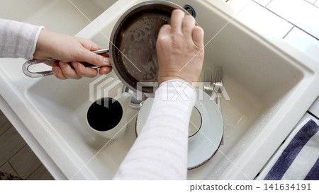 Man washes dishes in a kitchen sink Man washes dishes in a kitchen sink 141634191