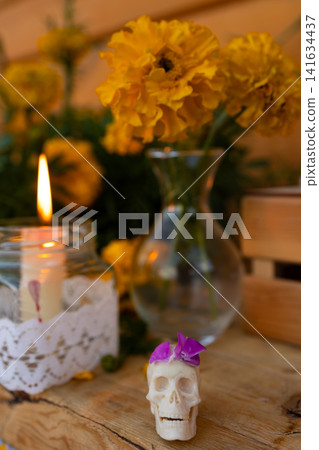 Decorative skull candle with purple flower beside glowing jar candle, yellow marigolds, lace wrap, rustic wood tabletop, soft bokeh background, festive memorial altar styling Decorative skull candle with purple flower beside glowing jar candle, yellow marigolds, lace wrap, rustic wood tabletop, soft bokeh background, festive memorial altar styling 141634437