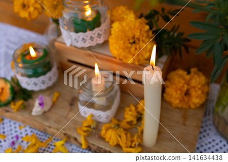 Candles and marigold blossoms arranged on rustic wooden altar, creating warm remembrance scene with soft glow, glass jars, foliage, and intimate handcrafted details 141634438