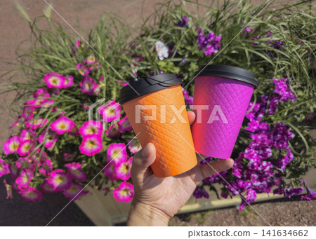Takeaway hot drinks in colorful corrugated paper cups in a person's hand outdoors. Summer coffee break, street cafe concept, vibrant lifestyle. Takeaway hot drinks in colorful corrugated paper cups in a person's hand outdoors. Summer coffee break, street cafe concept, vibrant lifestyle. 141634662
