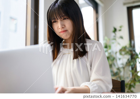 A Japanese woman is looking at her laptop in the office, deep in thought. A Japanese woman is looking at her laptop in the office, deep in thought. 141634770