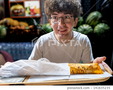 Istanbul, turkey. August 2, 2025. Young man holding a tray with two traditional turkish durum wraps, ready to eat street food in istanbul, turkey 141635235